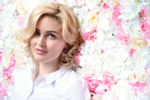 Beautiful 35-year-old woman stands against a floral wall with full cheeks from a dermal filler