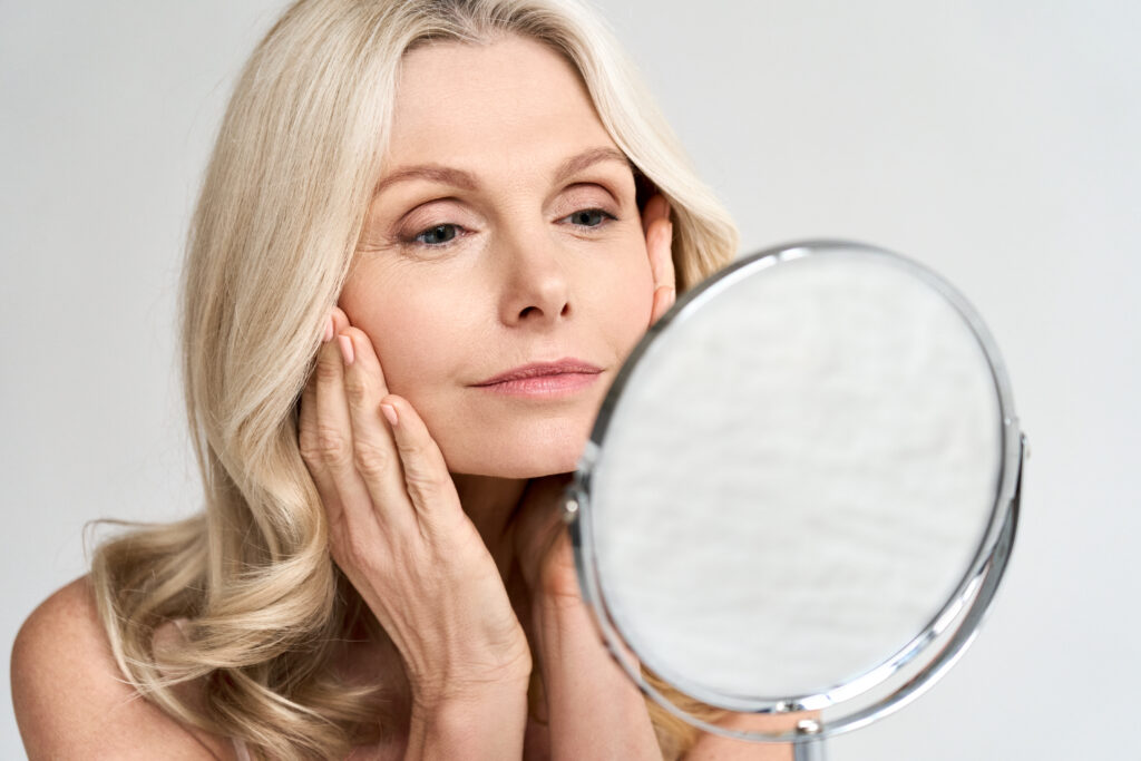 Woman examines her face in the mirror, looking for signs of aging